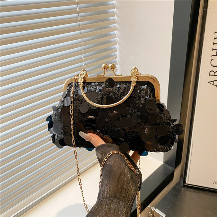 Black sequin handbag with gold handle and chain held by a person in front of a window.