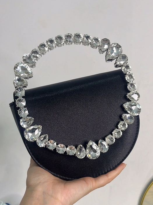 Black handbag with crystal handle held by a hand against a light gray background