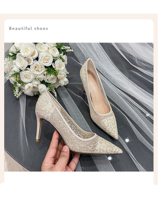Pair of beige high-heeled shoes held by a hand with white roses in the background
