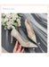 Pair of beige high-heeled shoes held by a hand with white roses in the background