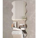A wavy, scalloped-edge wall mirror with a textured beige frame, shown mounted on a textured gray wall and reflecting a modern bedroom interior.