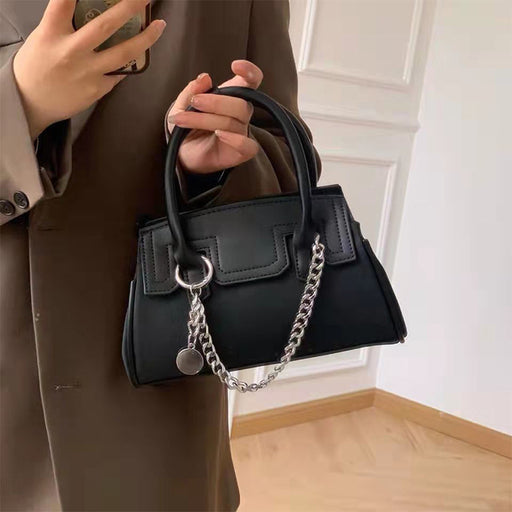 Person holding a black handbag with a chain detail indoors.