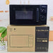 A black F. Blümlein microwave oven sits on top of its brown cardboard packaging box in a kitchen setting.