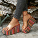 Colorful striped platform sandals worn with rolled-up jeans against a stone wall.