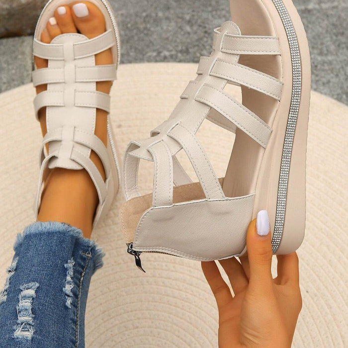 Beige strappy sandals with a platform held by a person wearing ripped jeans.