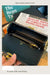 Black leather wallet with gold accents held open to show interior, on a desk with books and newspaper.