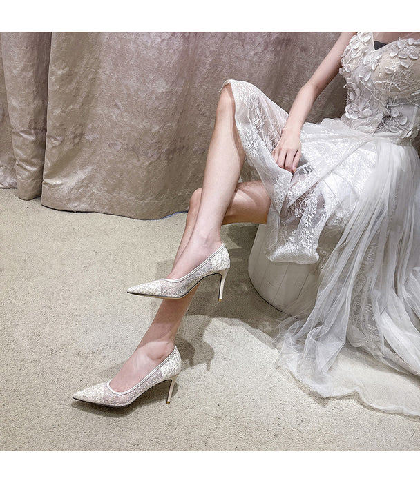 Woman in a white lace dress and sparkling high heels sitting on a beige surface.