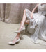 Woman in a white lace dress and sparkling high heels sitting on a beige surface.