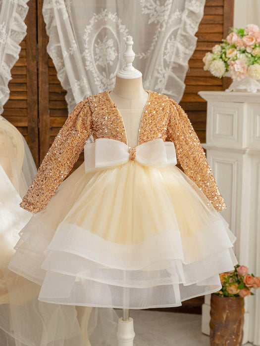 Children's dress with gold sequin jacket and white bow on a mannequin against a decorative background.