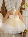 Children's dress with gold sequin jacket and white bow on a mannequin against a decorative background.