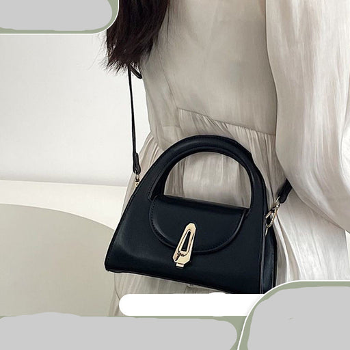 Black handbag with gold zipper held by a person against a neutral background