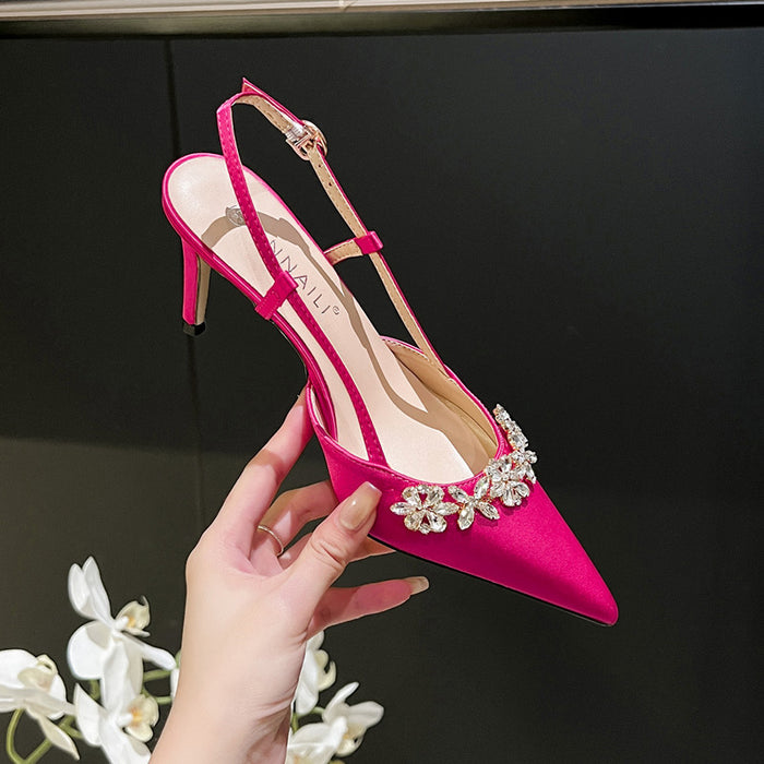 Pink high-heeled shoe with embellishments held by a hand against a dark background
