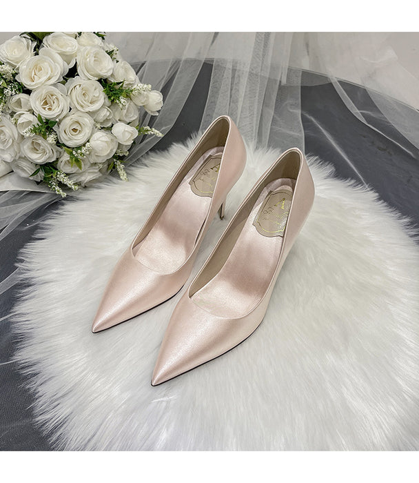 Pair of pink high-heeled shoes on a white fur surface with a bouquet of white roses in the background.