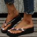 Black sandals with floral decorations on feet wearing jeans, against a neutral background