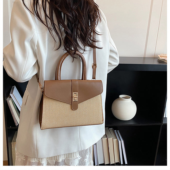 A woman from behind wearing a white blazer and carrying a structured handbag with a tan and beige woven body, brown leather top handle and flap, and a small gold clasp, set against an indoor background with a black shelf and a white vase.