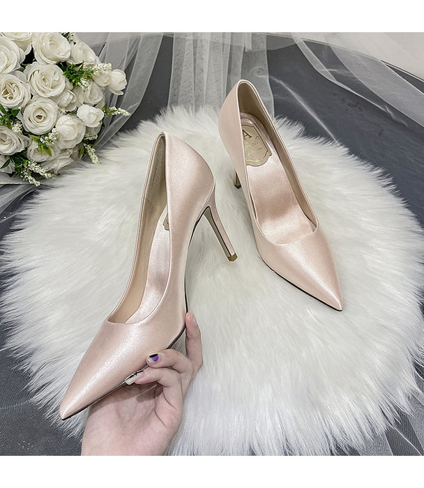 Pair of pink high-heeled shoes on a white fur surface with a bouquet of white flowers in the background.