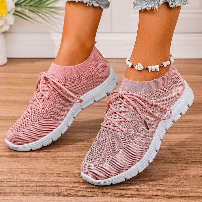 Pink sneakers with white soles worn on a wooden floor.