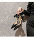 Black high-heeled shoes with bow and pearl detail held by a hand against a marble background