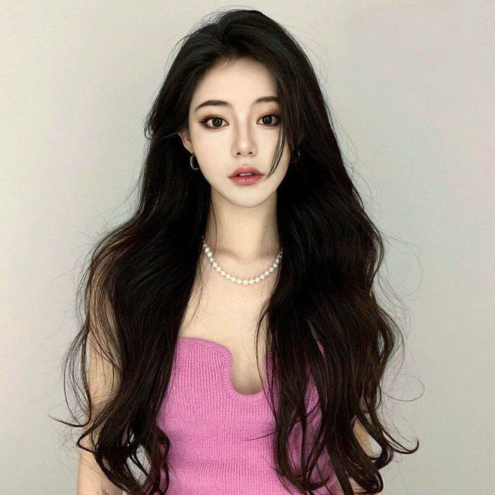 Woman with long dark hair wearing a pink top against a plain background