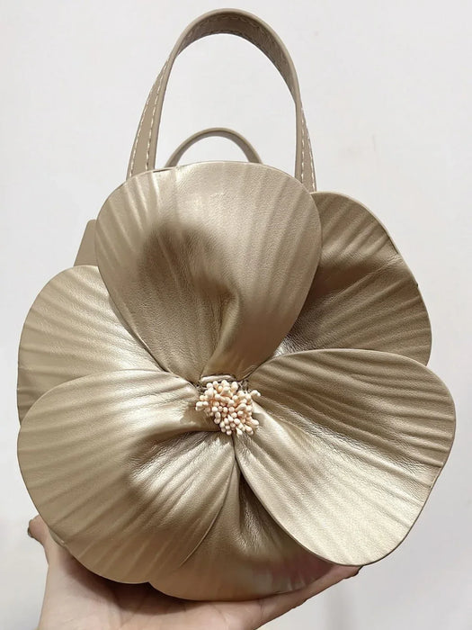 Beige handbag shaped like a flower with a pearl center held by a hand against a light background