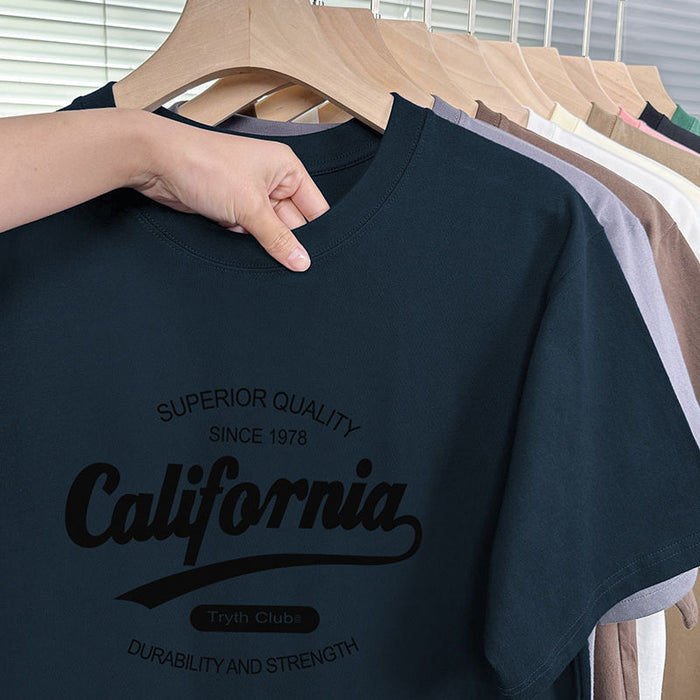 Black t-shirt with 'California' text held by a hand on a wooden hanger with other shirts in the background.