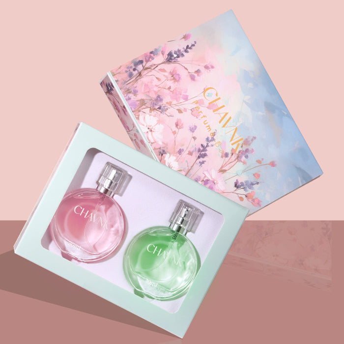 Two perfume bottles in a box with a floral design on the lid against a pink background