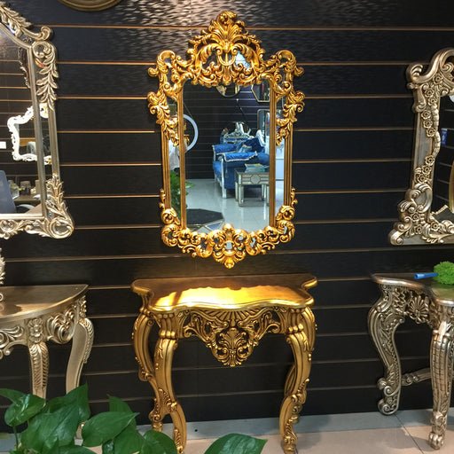 Decorative gold mirror and table against a black paneled wall.