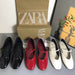 Four pairs of shoes in black, red, and white with Zara boxes in the background.