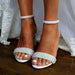 White sandals with silver embellishments on a wooden floor.