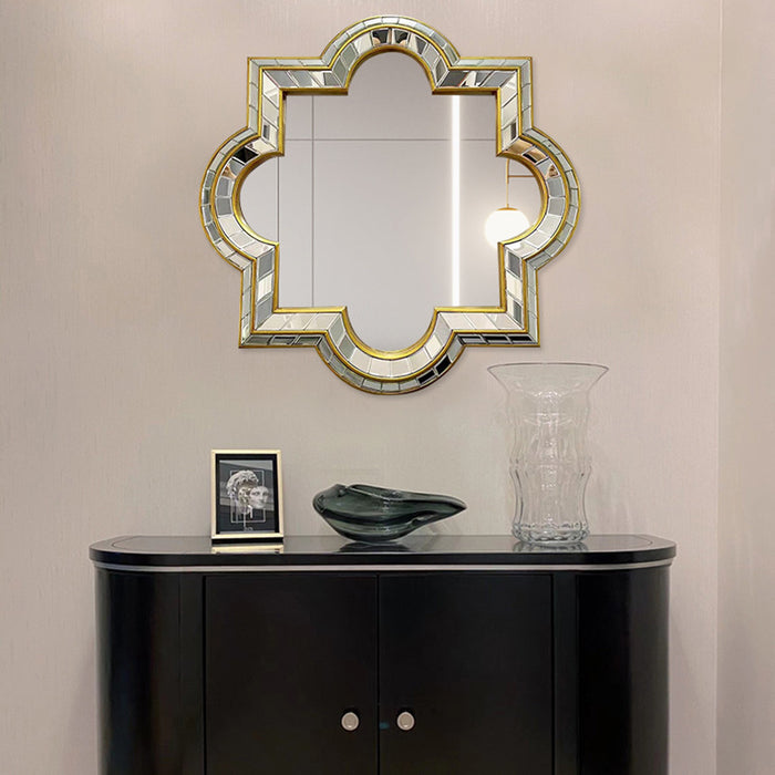 Decorative mirror with intricate frame above a black cabinet against a beige wall.