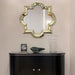 Decorative mirror with intricate frame above a black cabinet against a beige wall.