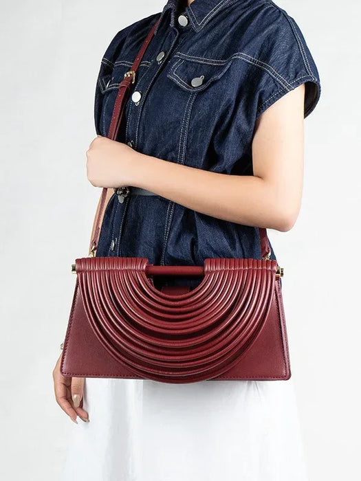 Person wearing a denim shirt holding a burgundy handbag against a white background