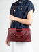Person wearing a denim shirt holding a burgundy handbag against a white background