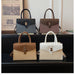 Four structured handbags with top handles and shoulder straps are arranged on a black shelf in an indoor setting. The bags come in four colorways: dark blue-gray, taupe-brown, tan, and off-white.