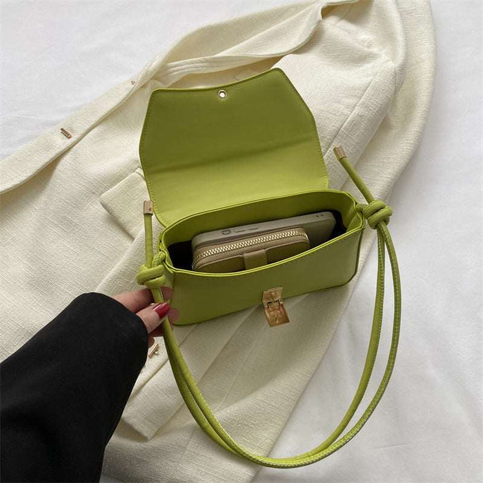 Green handbag held by a hand on a white background