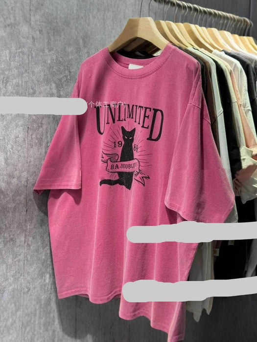 Pink t-shirt with graphic design on a hanger against a gray wall.