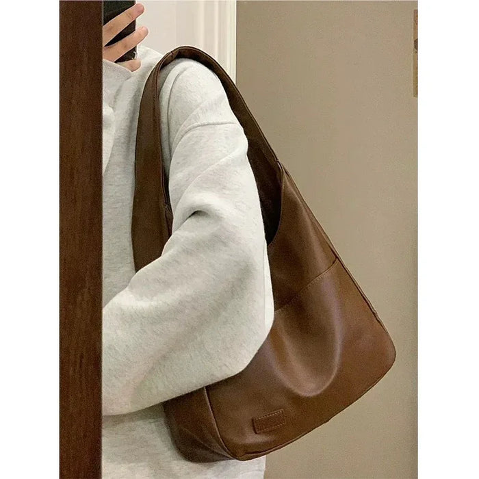 Person holding a brown leather handbag against a neutral background