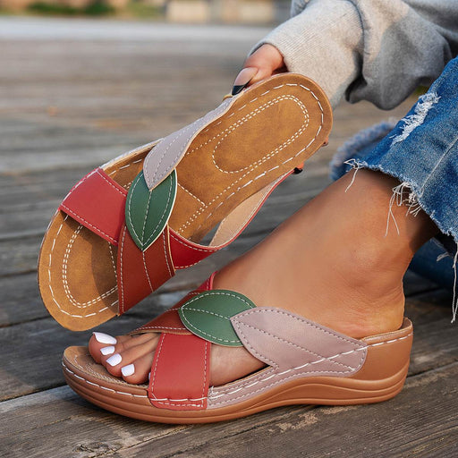 Colorful sandal with leaf details worn by a person on a wooden surface