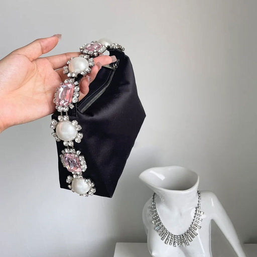 Hand holding a black clutch with decorative jewelry, next to a white mannequin head with a similar necklace.