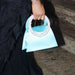 Hand holding a light blue handbag with decorative handle on a dark background