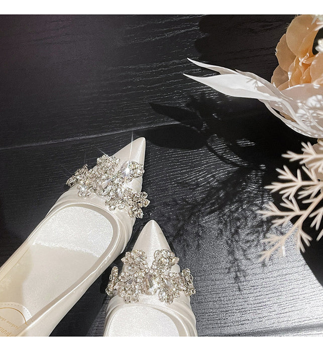 White wedding shoes with crystal embellishments on a dark surface with decorative elements.