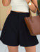 Person wearing black shorts with a white top and brown handbag.