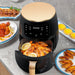 Black air fryer with digital display on a kitchen counter with cooked food around it.