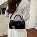 A woman wearing a light gray ribbed sweater and white skirt carries a black top-handle handbag with gold hardware and a gold FF logo clasp, photographed indoors in front of white cabinets.
