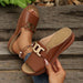 Brown sandals with gold buckles being held by a hand on a wooden surface.