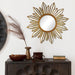 Decorative sunburst mirror on a wall above a wooden cabinet with decorative items.