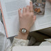 A close-up of a person's hand wearing a rose gold-toned watch with a round white dial, resting over an open book with printed text and a small food photo.