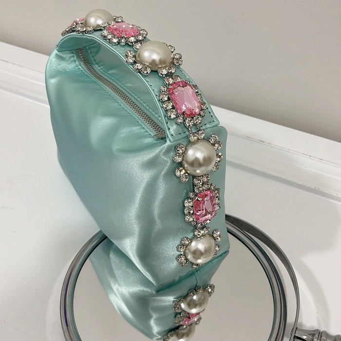 Teal satin headband with pearl and gemstone embellishments on a white surface.