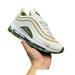 White sneaker with gold and green accents held in a hand against a white background