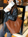 Person holding a brown leather handbag in an indoor setting